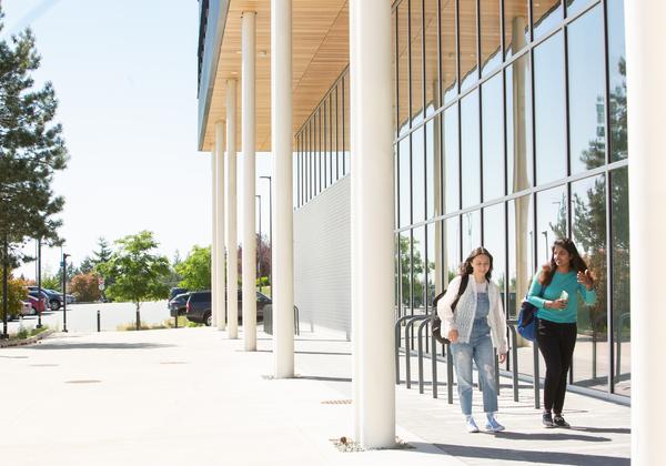 Two female students walking in front of a mirrored building