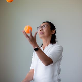 A woman with dark hair and glasses juggling.