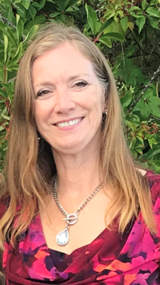 A woman smiling in a floral pink shirt and long, shoulder length hair.