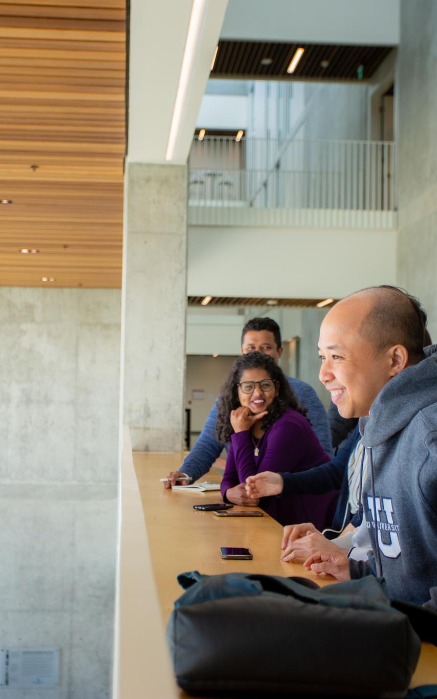 A few students standing at a railing overlooking an open space with a traditional totem in the background. 